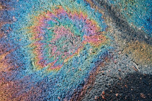 A beautiful colored shiny spot of oil, gasoline or diesel fuel on the wet asphalt. Leaked petroleum products on the roadway.