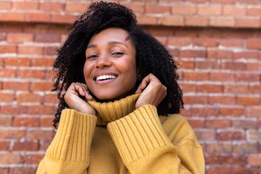 Portrait of African american woman looking at camera wearing yellow sweater. Orange brick background. Lifestyle concept.