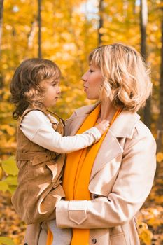 Woman with kid girl outdoors in fall. Child kissing mom. Mothers day holiday and autumn concept