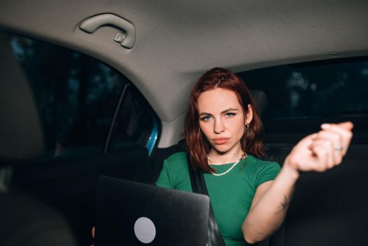 Beautiful woman is using a laptop and smiling while sitting on back seat in the car