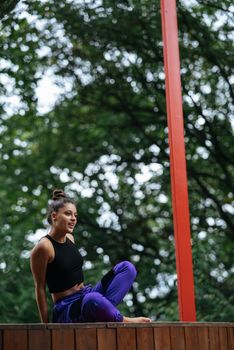Young woman is practising yoga sitting in the lotus position on a wooden podium in the garden