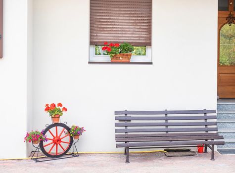 Traditional Alps front door. Wooden bench, flowers in pots and some kind of gentle decoration. Molveno region, Italy.