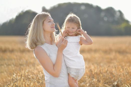 Mother holds daughter in her arms in a field with wheat Mothers day