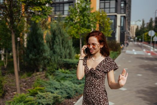 Beautiful woman is walking down the street with smartphone in her hands. Cute girl talking on mobile phone on modern city background