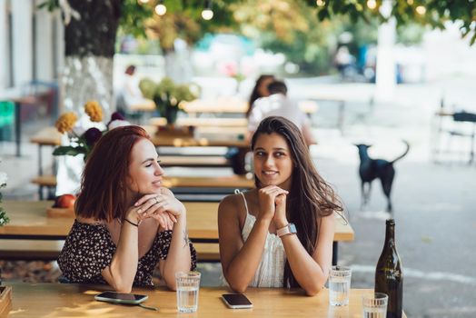Two young beautiful women girlfriends talking in an outdoor cafe, gossiping, telling news together. Female friendship