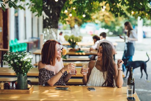 Two young beautiful women girlfriends talking in an outdoor cafe, gossiping, telling news together. Female friendship