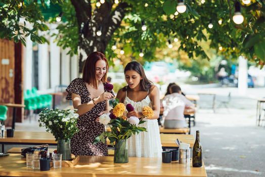 Two young women take orders and make up a beautiful festive bouquet. Floristry and making bouquets at the street caffe. Small business.