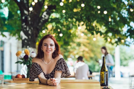 Close-up portrait of two female friends laughing drinking coffee on terrace at summer street cafe on background buildings