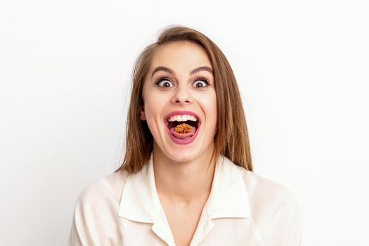 Happy young caucasian woman eating walnuts with an open mouth on white background with copy space