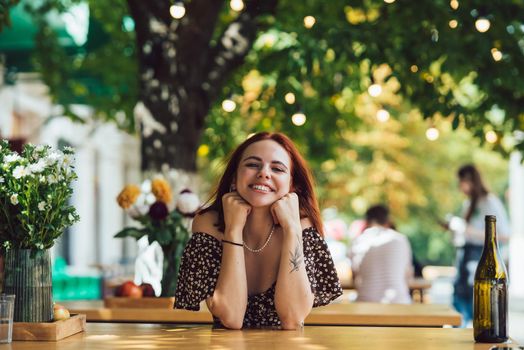 Close-up portrait of two female friends laughing drinking coffee on terrace at summer street cafe on background buildings