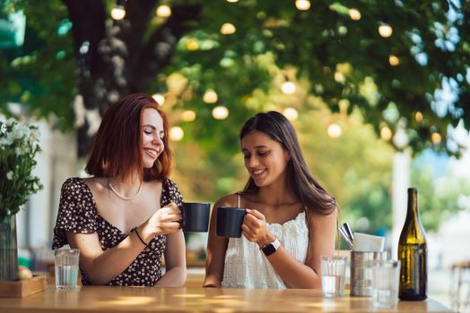 Two friends drinking coffee - women clinking with cups of coffee - female friendship concept