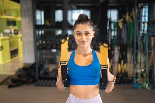 Young athletic woman with perfect body in sportswear doing exercises with trx fitness straps in the gym