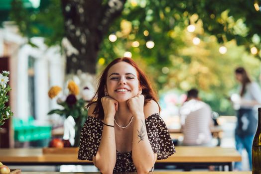 Close-up portrait of two female friends laughing drinking coffee on terrace at summer street cafe on background buildings