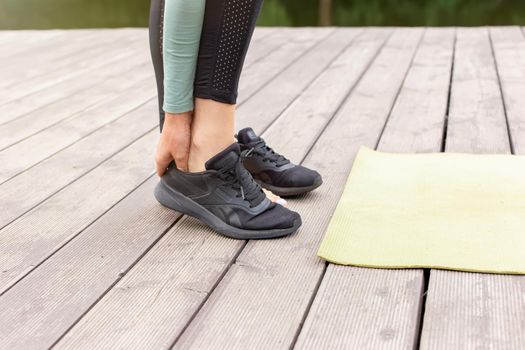 the feet of a girl taking off her black sneakers in front of a green sports mat lying on a wooden flooring, in the summer in the park. Copy space