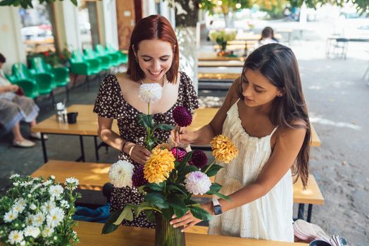 Two young women take orders and make up a beautiful festive bouquet. Floristry and making bouquets at the street caffe. Small business.