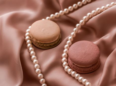 Girly, bakery and branding concept - Sweet macaroons and pearls jewellery on silk background, parisian chic jewelry, French dessert food and cake macaron for luxury confectionery brand, holiday gift