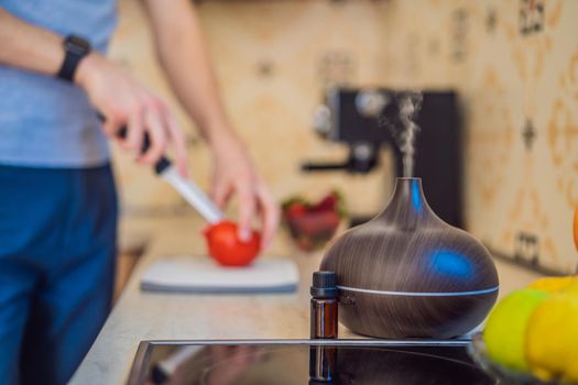 A man prepares food next to an aroma diffuser. cook cuts ripe red peppers in the kitchen. Cooking fresh, ripe, bell pepper salad for guests. Summer fresh vegetable salad.
