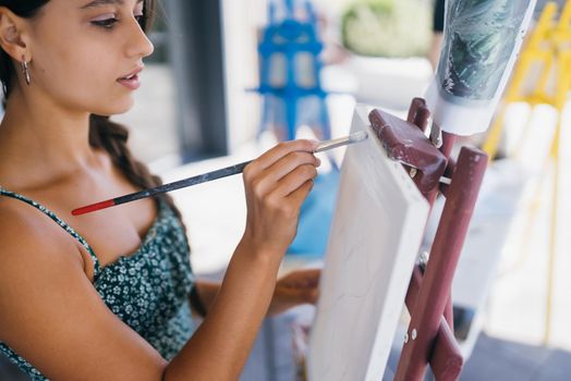 Beautiful woman artist drawing her picture on canvas with oil colors in studio