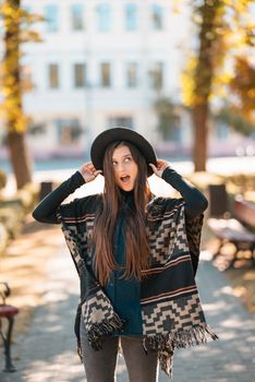 Stylish woman in poncho and hat enjoys autumn nature. People, freedom, lifestyle, travel and vacations concept.
