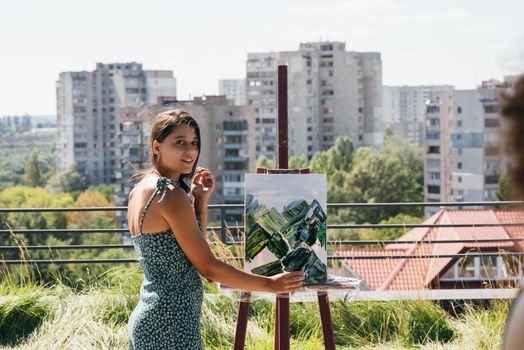 A young beautiful artist paints a picture against the background of the city
