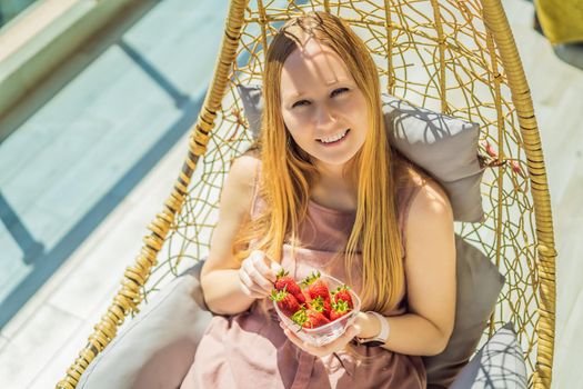 Portrait of gorgeous woman wearing beautiful dress sitting in a patio and eating strawberry.