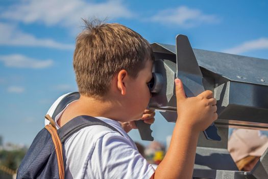 The boy looks through binoculars from the observation deck. Journey. Tourism