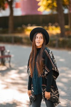 Stylish woman in poncho and hat enjoys autumn nature. People, freedom, lifestyle, travel and vacations concept.