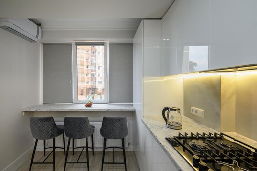 Interior of a modern white kitchen in a luxury studio apartment, chairs by the dining kitchen counter on the windowsill