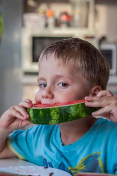 Cute boy eating watermelon at home. Real emotions without posing. children