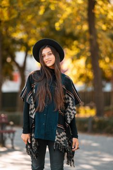Stylish woman in poncho and hat enjoys autumn nature. People, freedom, lifestyle, travel and vacations concept.