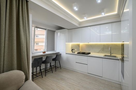 Interior of a modern white kitchen in a luxury studio apartment, chairs by the dining kitchen counter on the windowsill