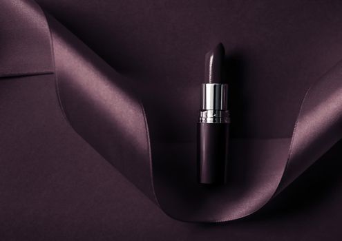 Cosmetic branding, glamour lip gloss and shopping sale concept - Luxury lipstick and silk ribbon on dark purple holiday background, make-up and cosmetics flatlay for beauty brand product design