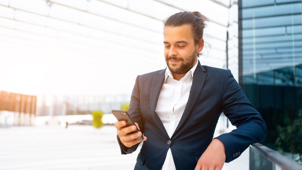 Businessman standing outdoor use smartphone looking device screen and smile. Handsome hispanic male business person middle age dressed business suit holding smartphone in hand. Modern business person