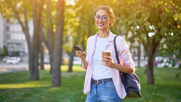 Businesswoman standing summer park Business person using smartphone Outdoors Successful european caucasian woman freelancer or teacher walking outside backpack dressed jeans white shirt pink jacket