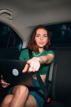 Beautiful woman is using a laptop and smiling while sitting on back seat in the car