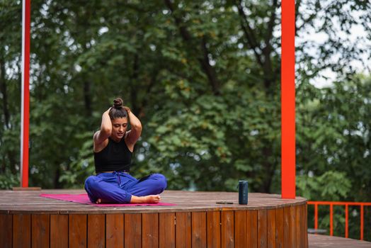 Young woman is practising yoga sitting in the lotus position on a wooden podium in the garden