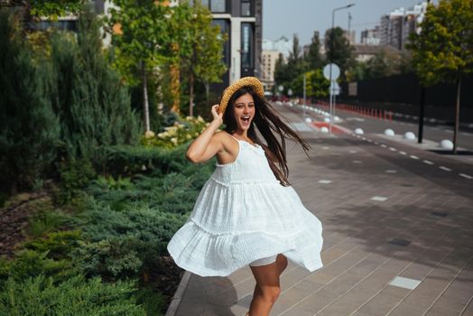 Young beautiful brunette woman in dress walking on the street, summer embankment outdoors