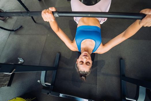 Beautiful woman doing exercises with barbell on a bench press training in a fitness center