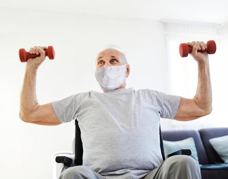 Happy senior man in wheelchair wearing protective mask exercising at home or nursing home
