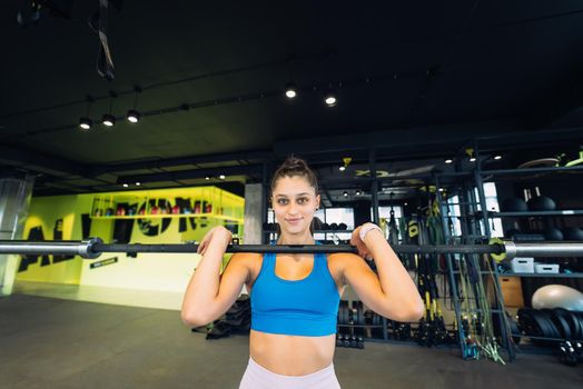 Beautiful and strong young woman doing sit-ups with a barbell for growth of buttocks.