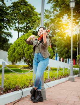 Woman playing violin in the street. Portrait of violinist girl playing in the street. Woman artist playing violin outdoors, Girl lying down playing violin in a park