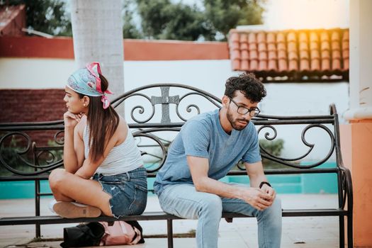 Unhappy couple sitting back to back on bench. Concept of couple problems and crisis. Upset young couple sitting back to back in a park, Young couple arguing sitting back to back on a bench