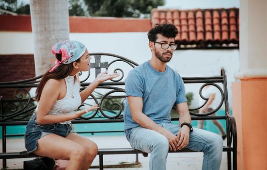 Couple sitting on a park bench arguing. A young couple arguing sitting in a park, Concept of aggressive couples in the park. Upset couple arguing on park bench