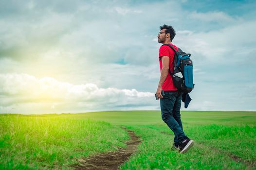 Side view of backpacking man on a beautiful road in the countryside. Young explorer man walking in a green field, Backpacker man walking in a beautiful field.