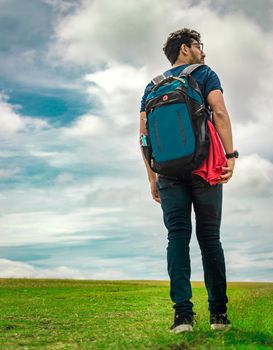 Low angle of traveler man walking in the field. Backpacker man walking in the countryside. Young traveler man walking in green field. Lifestyle of adventurous man in the field