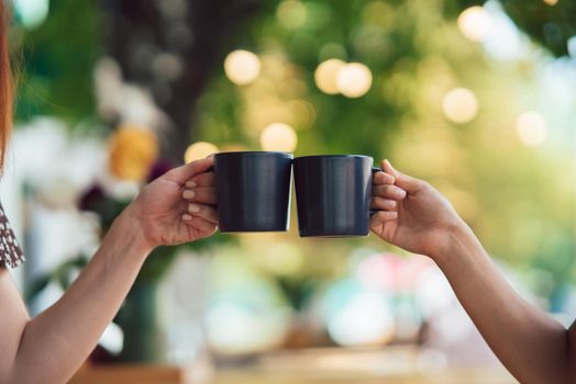 Closeup image of a couple people clinking coffee cups together in cafe