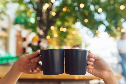 Closeup image of a couple people clinking coffee cups together in cafe