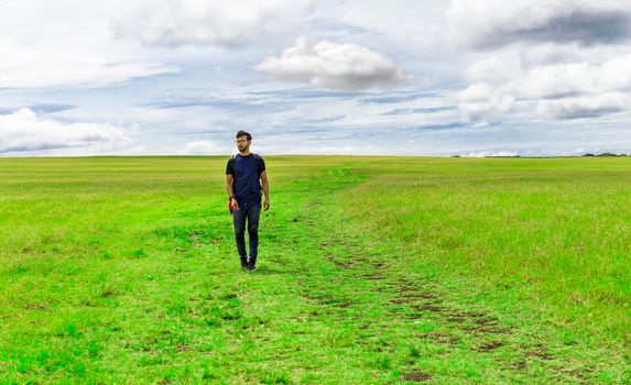 Traveler man walking in the beautiful countryside. Backpacker man walking in a countryside. Landscape of traveler man walking in the green field. Lifestyle of adventurous man in the field