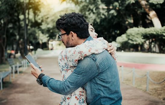 Unfaithful man hugging his girlfriend and looking at the cell phone. Concept of unfaithful man using cell phone. Unfaithful man looking at the cell phone while hugging his girlfriend outdoors