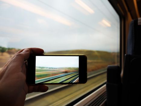 subjective shot of the hand of a person taking a picture with his smart phone, is photographing the landscape seen through the window of the train